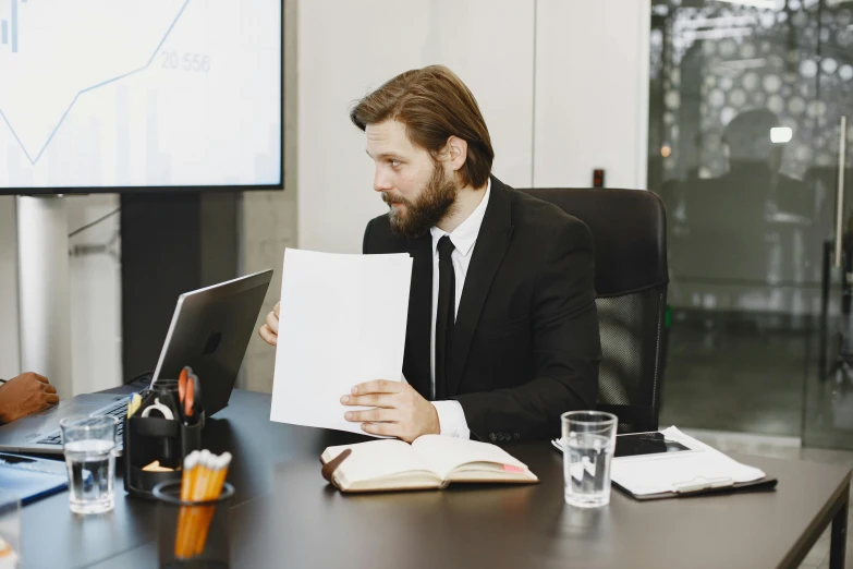 a man sitting at a table in front of a laptop computer, a photocopy, by Adam Marczyński, pexels contest winner, wearing a black suit, holding a clipboard, lachlan bailey, max bedulenko