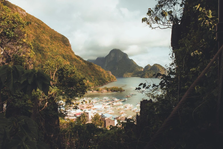 a large body of water next to a lush green hillside, by Daniël Mijtens, pexels contest winner, fishing village, 1970s philippines, warm glow, grey