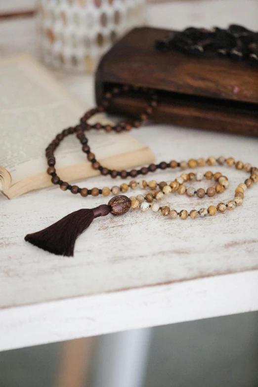 a rosary and a book on a table, by Helen Stevenson, unsplash, dressing tassels gemstones, brown and cream color scheme, padmasana, made of wood