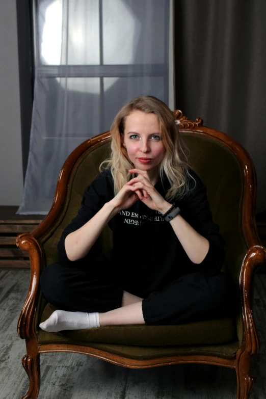 a woman sitting in a chair in front of a window, a portrait, inspired by Anna Füssli, pexels contest winner, wearing a black shirt, russian academic, a blond, in a dark studio room