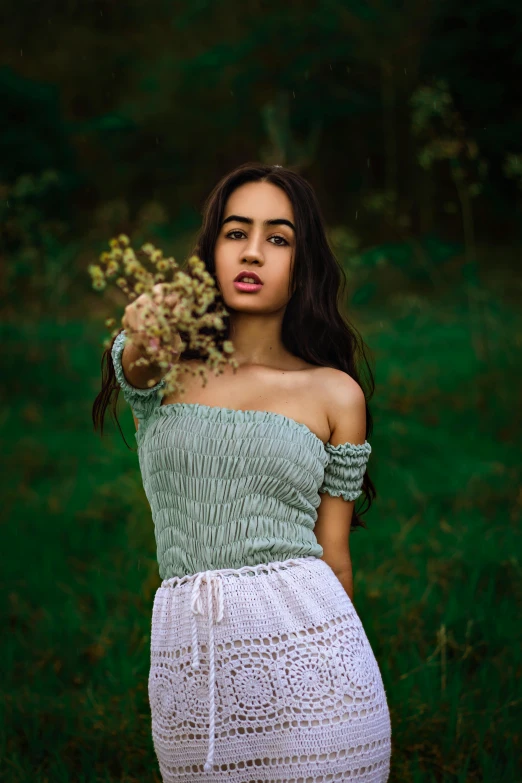 a woman standing in a field holding a bunch of flowers, inspired by Elsa Bleda, pexels contest winner, renaissance, portrait of vanessa morgan, wearing a cropped top, green clothes, isabela moner