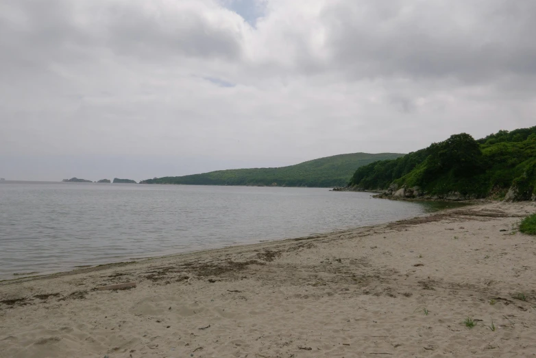 a sandy beach next to a body of water, grey skies, bay, slightly sunny, notan