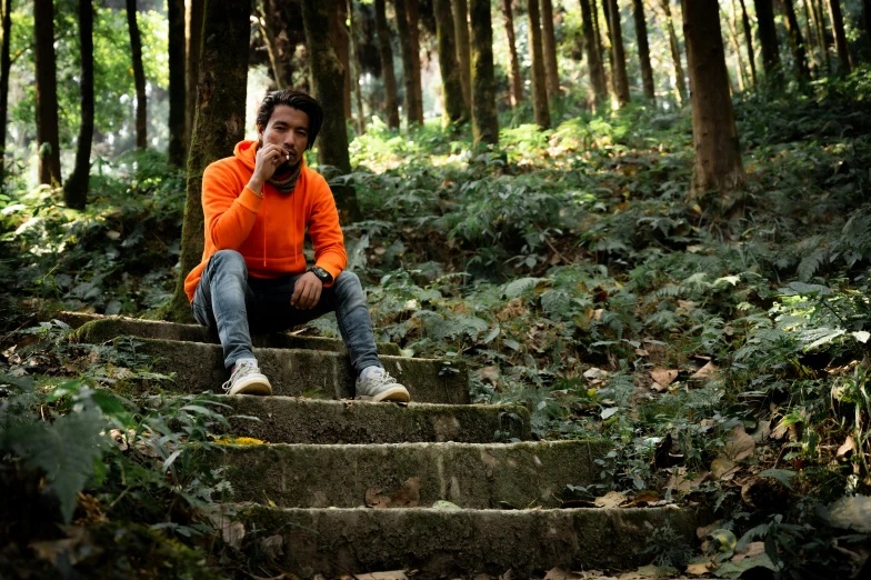 a man sitting on some steps in the woods, a portrait, pexels, sumatraism, orange hoodie, avatar image, alone!!, smoking