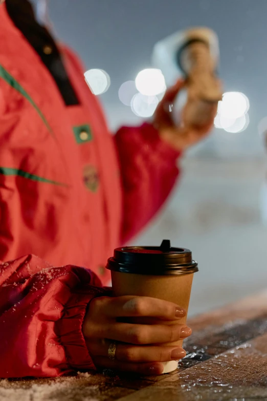 a close up of a person holding a cup of coffee, night-time, wearing festive clothing, hooded, cardboard