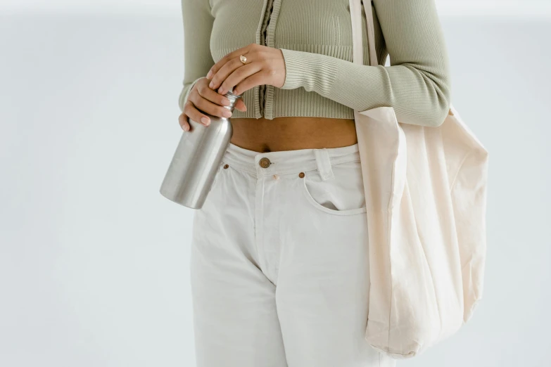 a woman holding a water bottle and a bag, by Matija Jama, trending on pexels, minimalism, white pants, her belly button is exposed, holding a tin can, silver，ivory