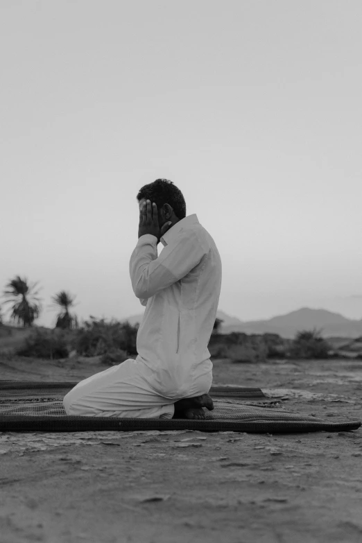a man sitting on a surfboard on the beach, a black and white photo, by Ahmed Yacoubi, unsplash, hurufiyya, praying posture, upset, in desert, movie still of a tired