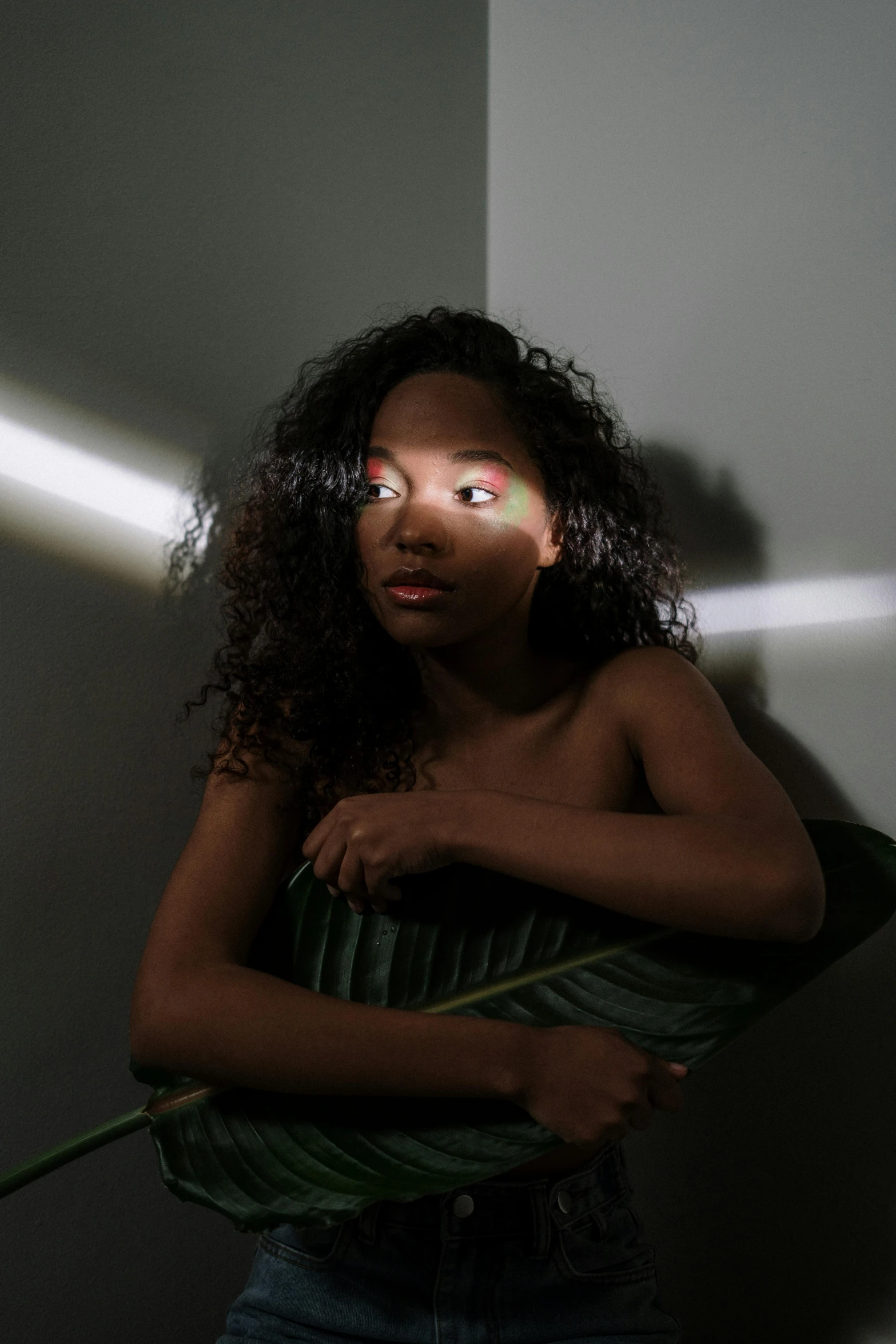 a woman holding a flower in front of a wall, an album cover, by Lily Delissa Joseph, glowing with silver light, looking towards the camera, light entering through a blind, dark-skinned