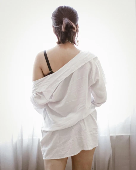 a woman standing in front of a window, open shirt, showing her shoulder from back, wearing white pajamas, promo image