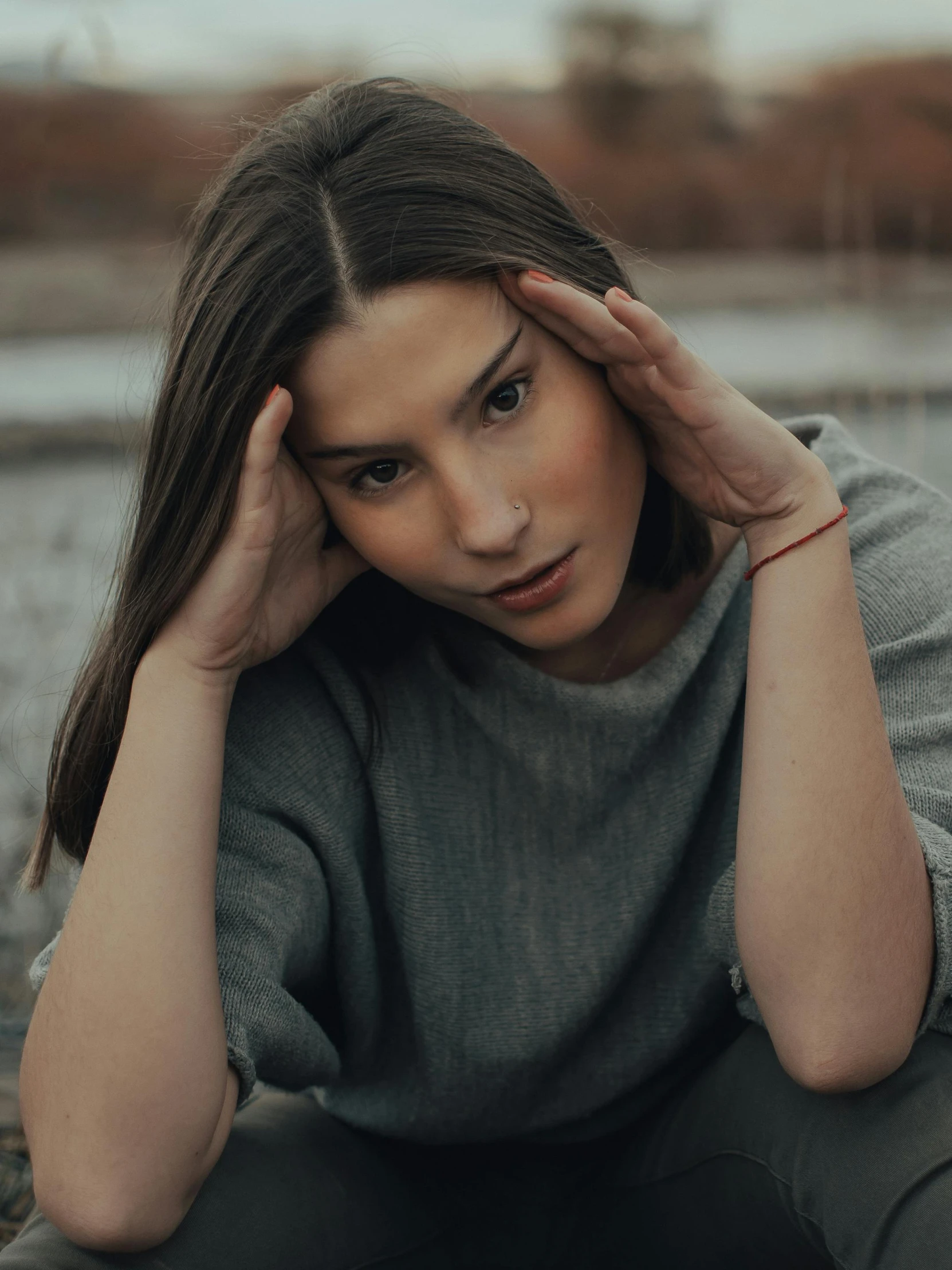 a woman sitting on the ground with her hands on her head, trending on pexels, grey sweater, 🤤 girl portrait, quiet beauty, half image