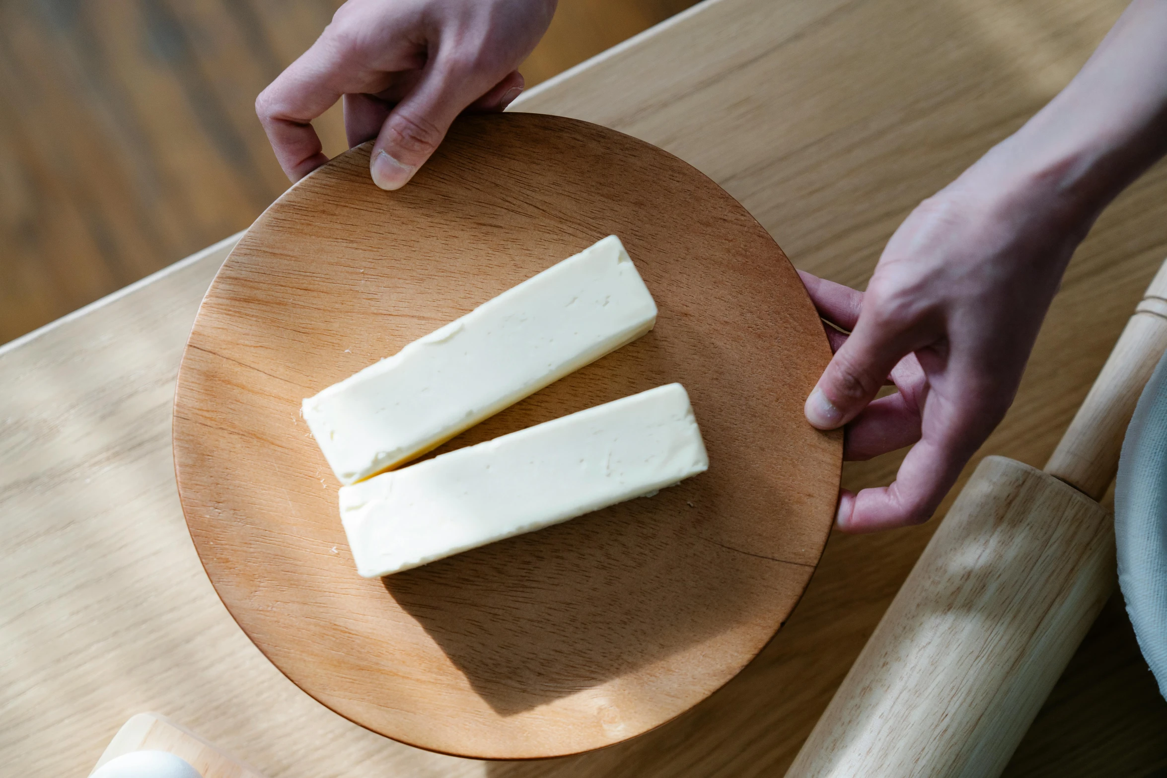 a person cutting a piece of cheese on a wooden plate, by Jessie Algie, rectangular, cream, long, close together