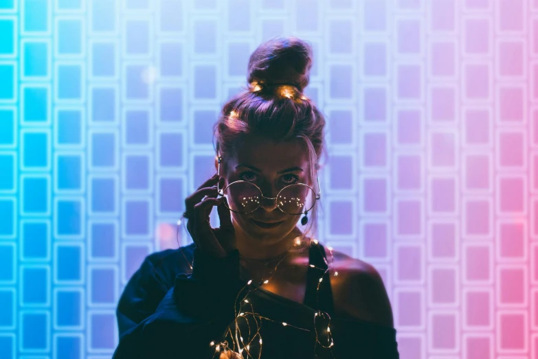 a woman holding a cell phone to her ear, a picture, inspired by Elsa Bleda, trending on pexels, holography, party lights, girl wearing round glasses, topknot, portrait mode photo