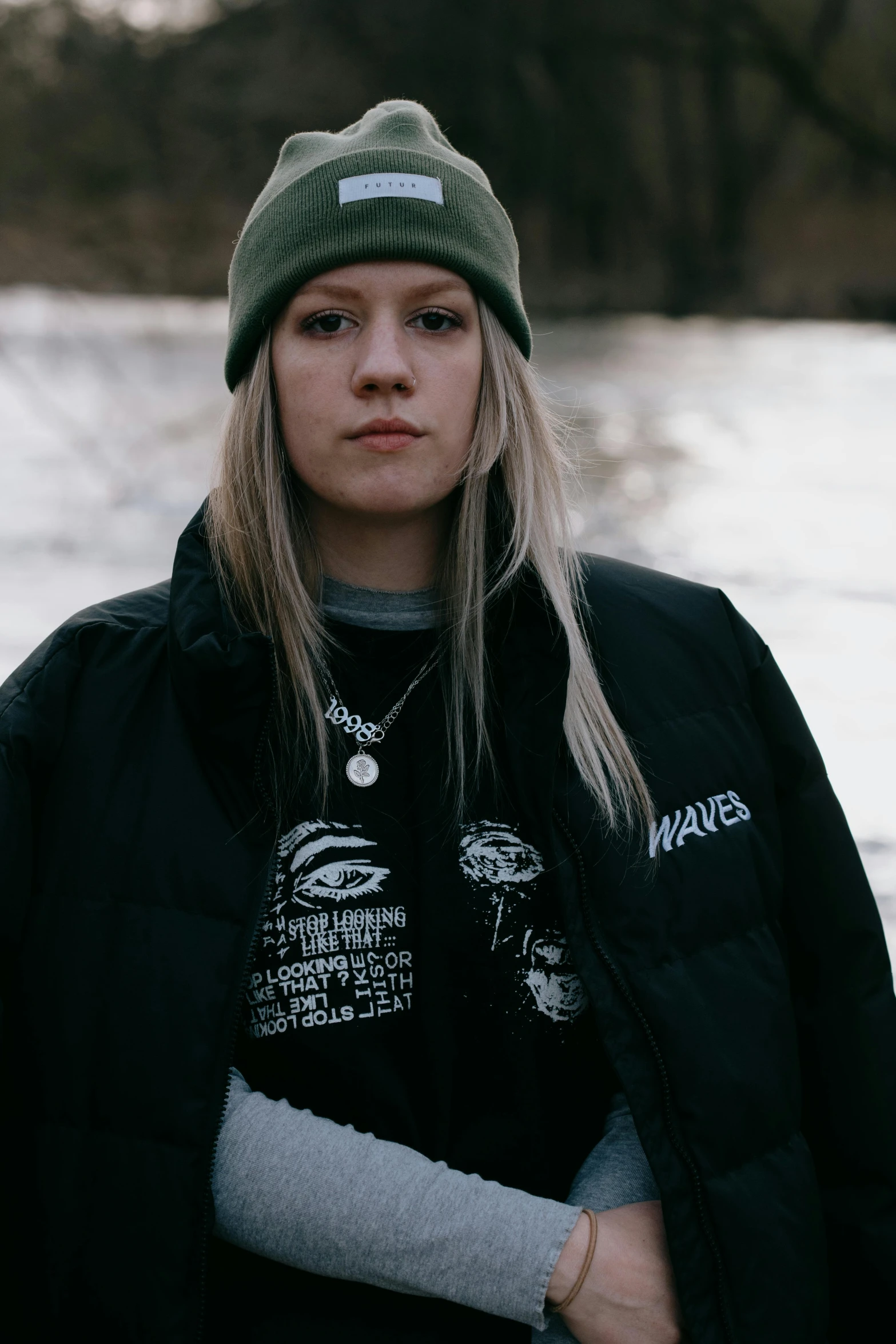 a woman standing in front of a body of water, an album cover, inspired by Elsa Bleda, trending on pexels, graffiti, black beanie, sydney sweeney, angry look, black jacket