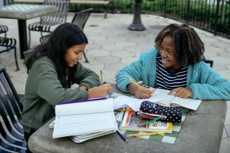 two girls sitting at a table with books and pencils, by Loren Munk, pexels contest winner, in a city square, mathematics unifying science, alexis franklin, character sheets on table