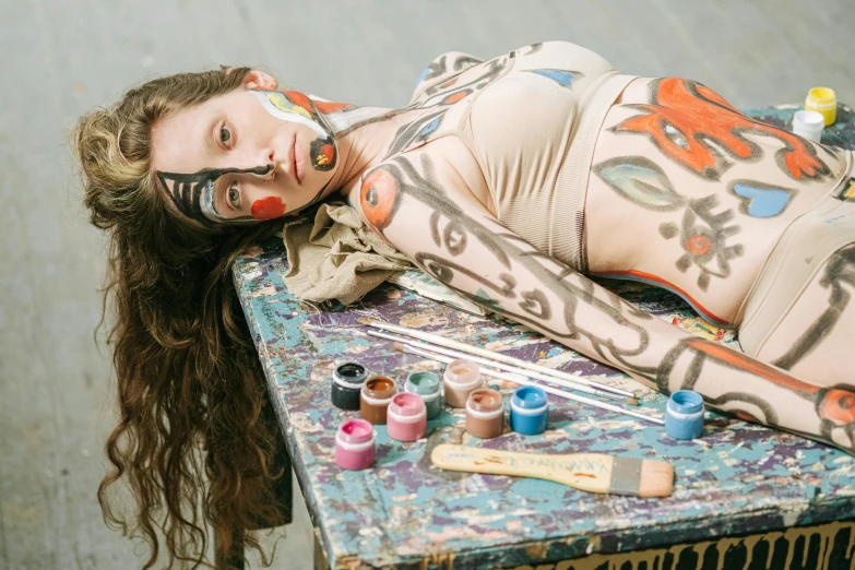 a woman laying on top of a table covered in paint, inspired by Francesco Clemente, trending on pexels, skintight suits, portrait sophie mudd, gustav klimt 4 k, cottagecore hippie