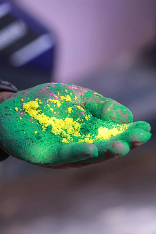 a person with green and yellow paint on their hands, full of sand and glitter, heavy pigment, commercially ready, handheld