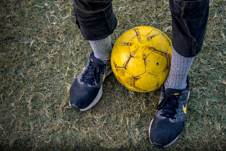 a person standing next to a yellow soccer ball, by Matt Cavotta, pexels contest winner, focus on his foot, avatar image, well worn, schools