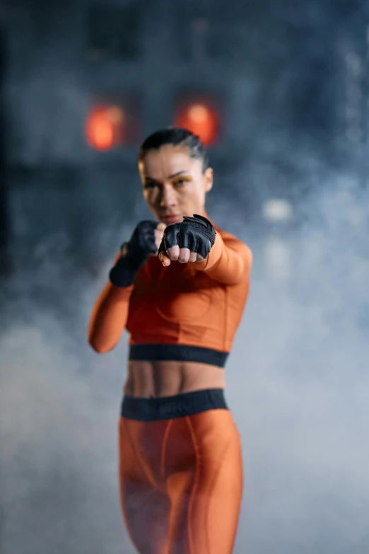 a woman in an orange outfit holding a gun, pexels contest winner, mma southpaw stance, female cyborg in data center, avatar image, strong fighter in leathers