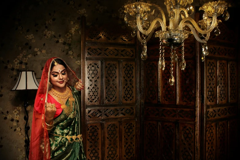 a woman in a green and red dress standing in front of a chandelier, inspired by Raja Ravi Varma, hurufiyya, wedding, official store photo, [ cinematic, sari