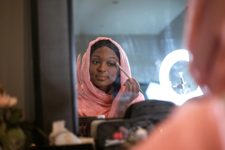 a woman putting on makeup in front of a mirror, by Arabella Rankin, hurufiyya, hijab, shot on sony a 7 iii, brown skin. light makeup, performing