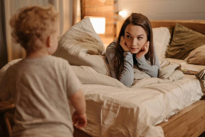 a woman sitting on top of a bed next to a child, pexels contest winner, annoyed, good morning, intense flirting, brown