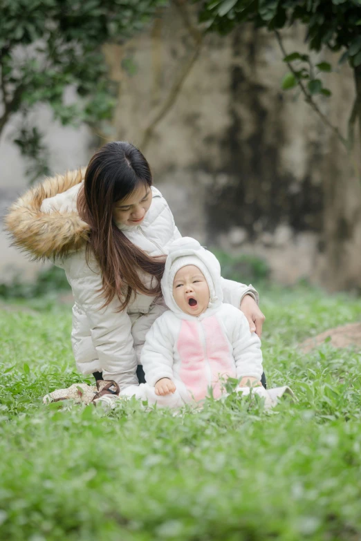 a woman sitting on top of a lush green field next to a baby, inspired by Cui Bai, pexels contest winner, wearing a white winter coat, shanghai, licking, avatar image