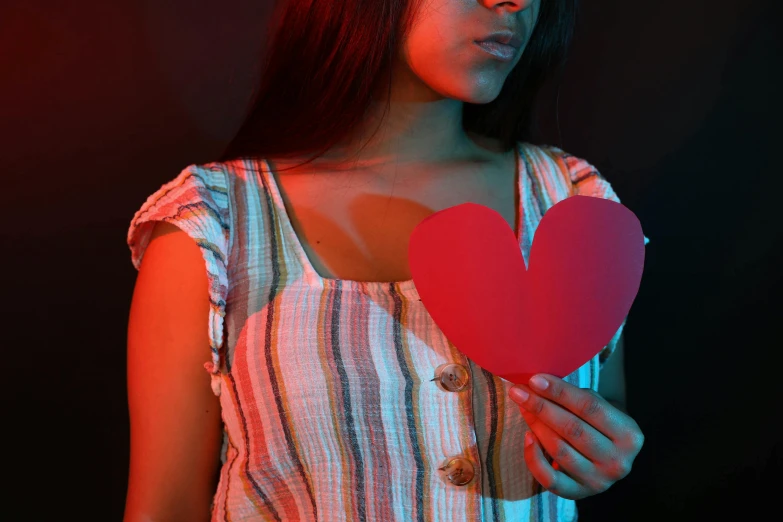 a woman holding a paper heart in front of her face, an album cover, pexels, red and blue back light, indian girl with brown skin, sad and lonley, ( ( dark skin ) )