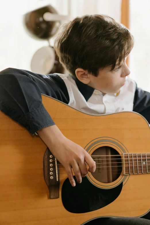 a young boy sitting on a couch playing a guitar, an album cover, trending on pexels, looking her shoulder, school class, thumbnail, organic detail