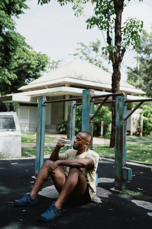 a man sitting on a bench in a park, frank ocean, dingy gym, drinking, set on singaporean aesthetic