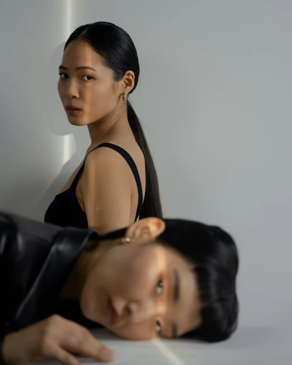 a man and a woman standing next to each other, an album cover, inspired by Wang Duo, trending on pexels, photorealism, queer woman, asian girl, looking in mirror, modeling studio