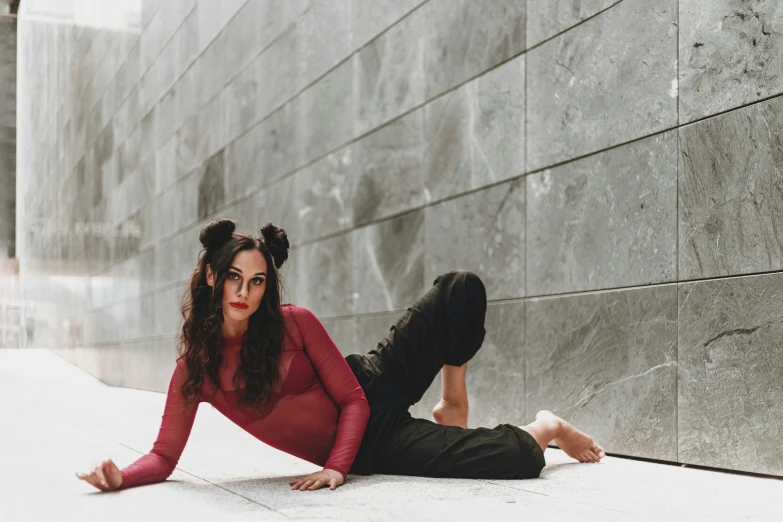 a woman laying on the ground in front of a wall, by Nina Hamnett, pexels contest winner, bauhaus, brunette fairy woman stretching, brown hair in two buns, cruella devil, wearing a tracksuit