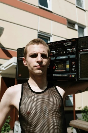 a man standing in front of a building holding a boombox, by Attila Meszlenyi, reddit, no shirt under the vest, huge earrings and queer make up, vitalik buterin, portrait shot 8 k