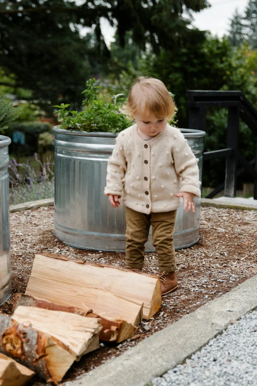 a little boy standing next to a pile of wood, inspired by Elsa Beskow, unsplash, wearing a cardigan, walking at the garden, full product shot, fire pit