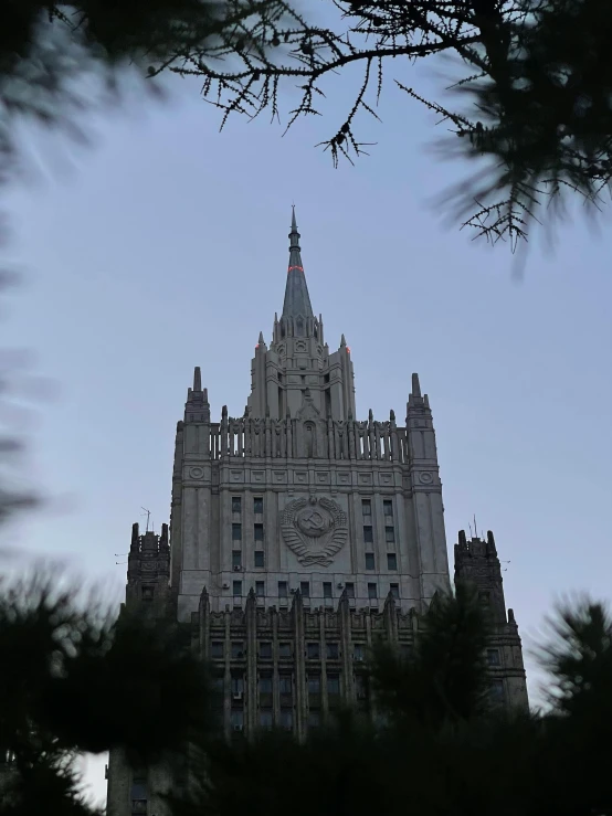 a very tall building with a clock on it's face, an album cover, by Miroslava Sviridova, unsplash, modernism, russian national guard, city buildings on top of trees, captured in low light, devil's horns