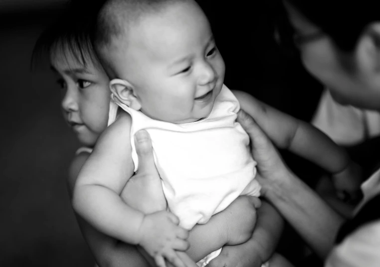 a woman holding a baby in her arms, a black and white photo, pexels, happening, ruan jia and brom, brothers, happy face, digitally enhanced