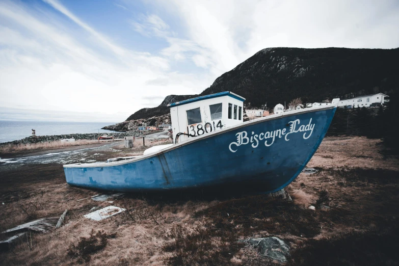 a blue boat sitting on top of a sandy beach, inspired by Bascove, unsplash contest winner, graffiti, gloomy skies, francois legault, dressed in a worn, fishing