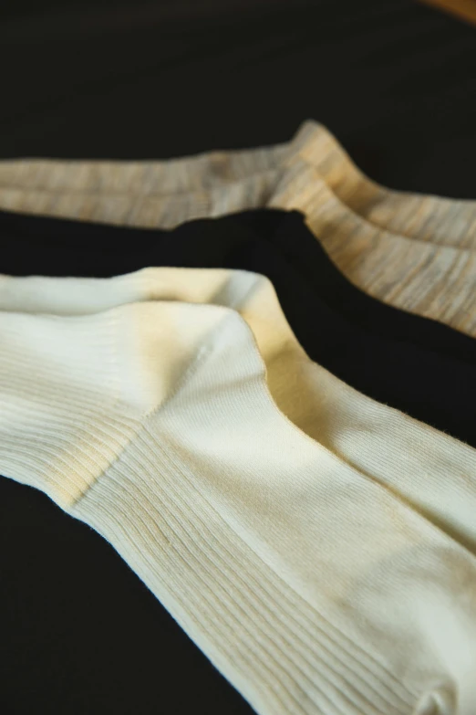 three pairs of socks sitting on top of a bed, by Thomas Barker, unsplash, renaissance, double layer fold over hem, ivory and ebony, detail shot, organic detail