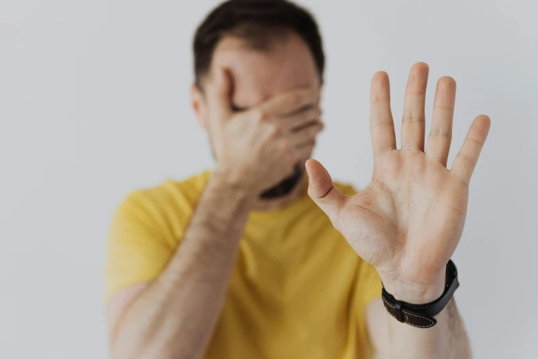 a man covering his face with his hands, trending on pexels, wearing a modern yellow tshirt, ptsd, stripe over eye, raised hand