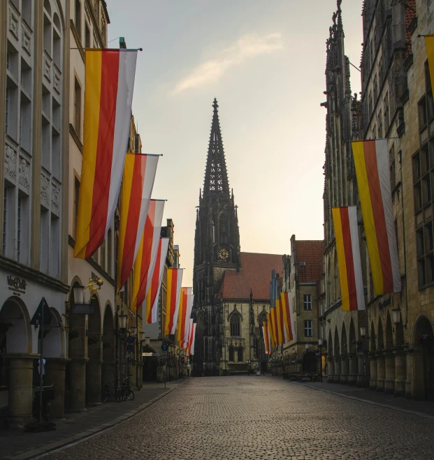 a street filled with lots of flags next to tall buildings, by Matthias Stom, pexels contest winner, renaissance, gothic church background, red and yellow light, square, germany. wide shot