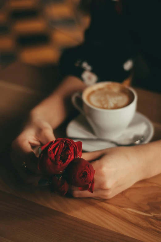 a person sitting at a table with a cup of coffee, inspired by Elsa Bleda, romanticism, holding a red rose, two cups of coffee, profile image, sitting on a mocha-colored table