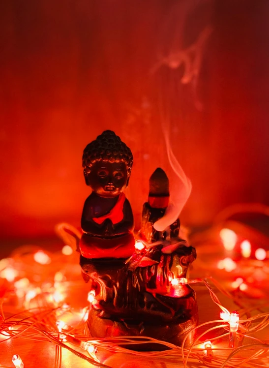 a small figurine sitting on top of a pile of lights, mangeta smoke red light, cosy vibes, buddha, high-quality photo