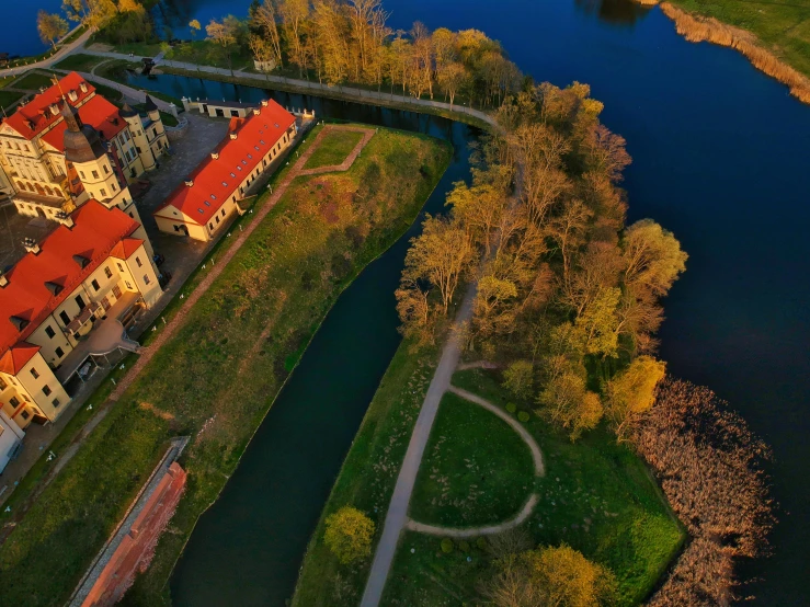 a large building sitting on top of a lush green field, by Adam Marczyński, pexels contest winner, renaissance, close river bank, warm glow, fpv, full frame image