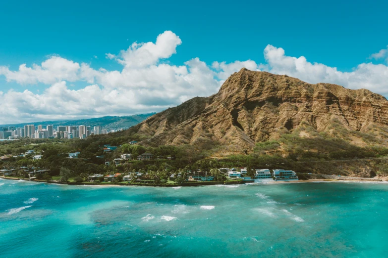 a beach with a mountain in the background, by Drew Tucker, pexels contest winner, waikiki beach, aerial view of an ancient land, frank lloyd wright, trees and cliffs