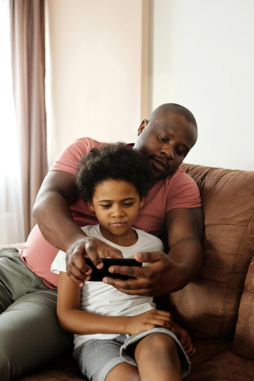 a man and a little girl sitting on a couch, looking at his phone, dark-skinned, game ready, comforting