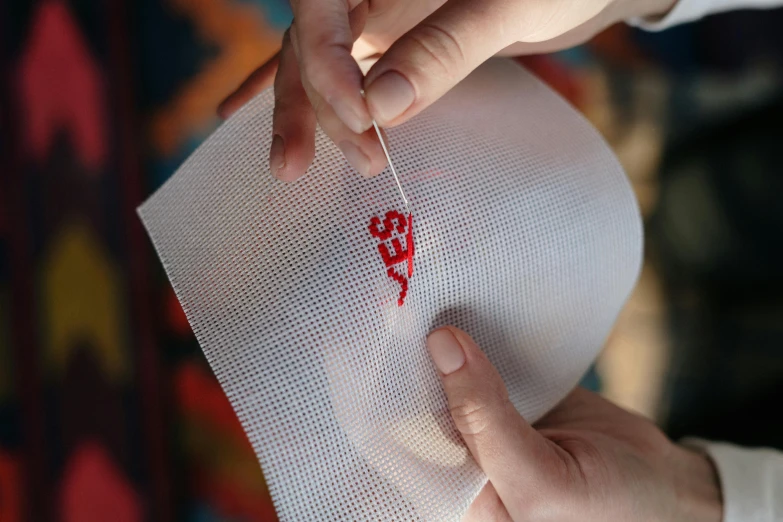 a close up of a person holding a piece of cloth, a cross stitch, white red, letter s, 3 5 °, product shot