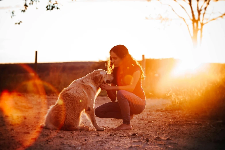 a woman kneeling next to a dog on a dirt road, by Julia Pishtar, pexels contest winner, sunset backlight, aussie, warm coloured, various posed