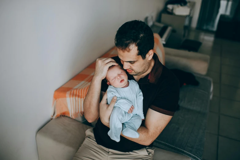 a man sitting on a couch holding a baby, pexels contest winner, avatar image, caring fatherly wide forehead, indoor picture, profile image