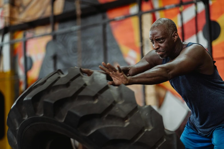 a man holding a large tire in a gym, a portrait, pexels contest winner, emmanuel shiru, tapping in to something greater, ninja warrior, working out in the field