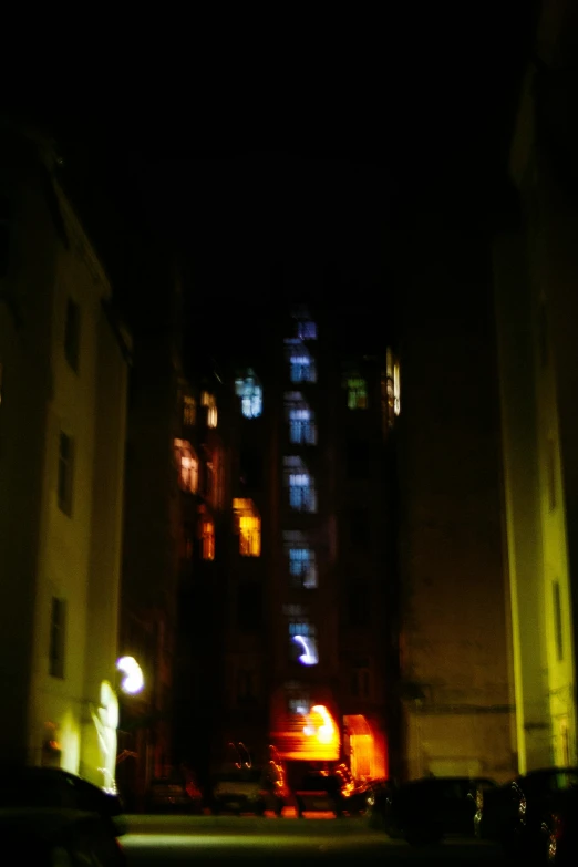 a city street at night with a building in the background, holography, gotic harts, low quality photo, little windows, nighttime!!