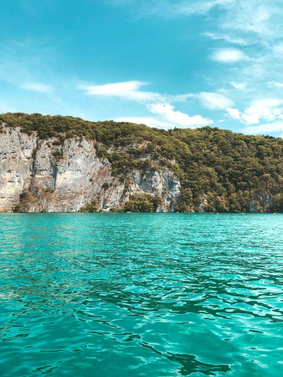 a body of water with a mountain in the background, turquoise blue face, chalk cliffs above, lush surroundings, 4k image”