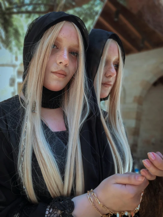 a couple of women standing next to each other, an album cover, inspired by INO, unsplash, renaissance, platinum blonde long hair, wearing a dark hood, adult pair of twins, photo taken in 2 0 2 0